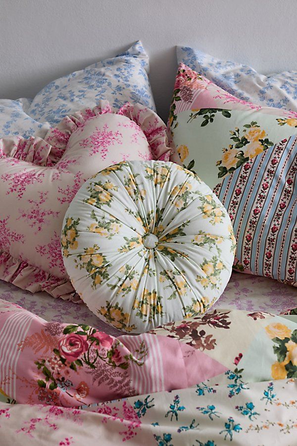 a bed with many pillows on it and one pillow has a flowered design in the middle