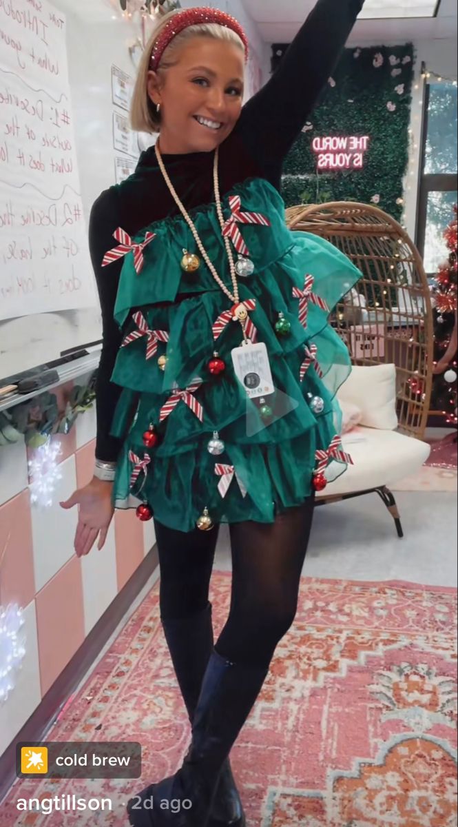 a woman wearing a green dress and black tights is standing in front of a christmas tree