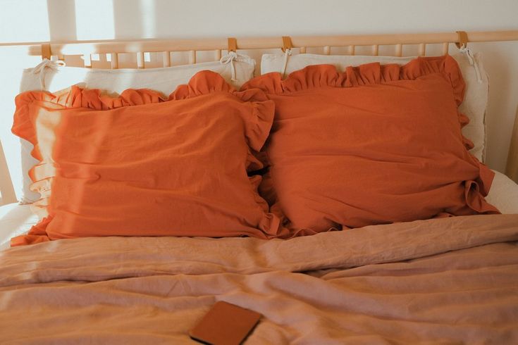 two orange pillows sitting on top of a bed next to a pillow case and blanket