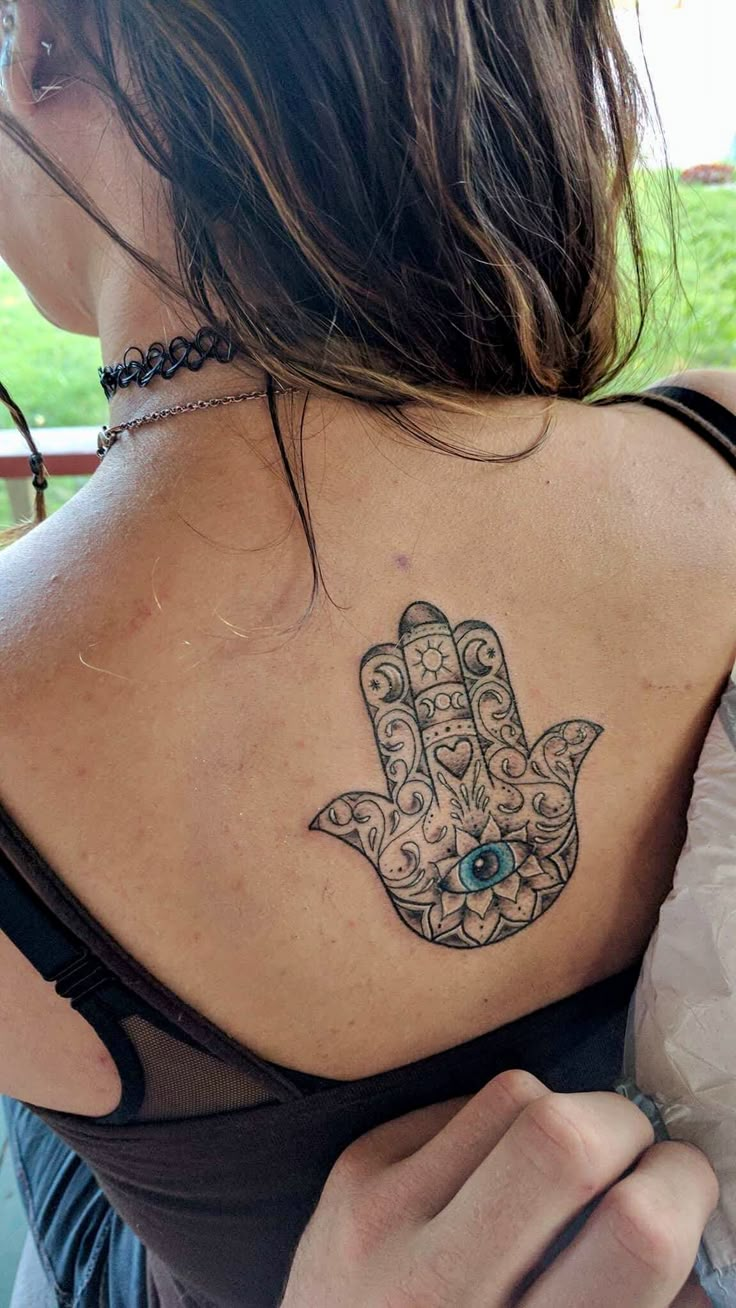 a woman with a hamsa tattoo on her upper back and shoulder, holding onto the arm