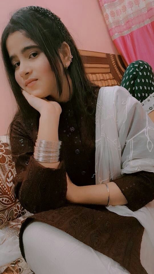 a young woman sitting on top of a bed next to a pink wall and holding her hand under her chin