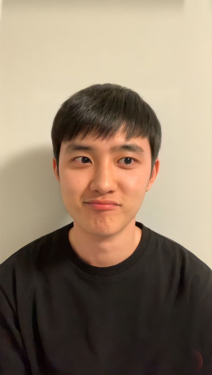 a young man is posing for the camera in front of a white wall and wearing a black t - shirt