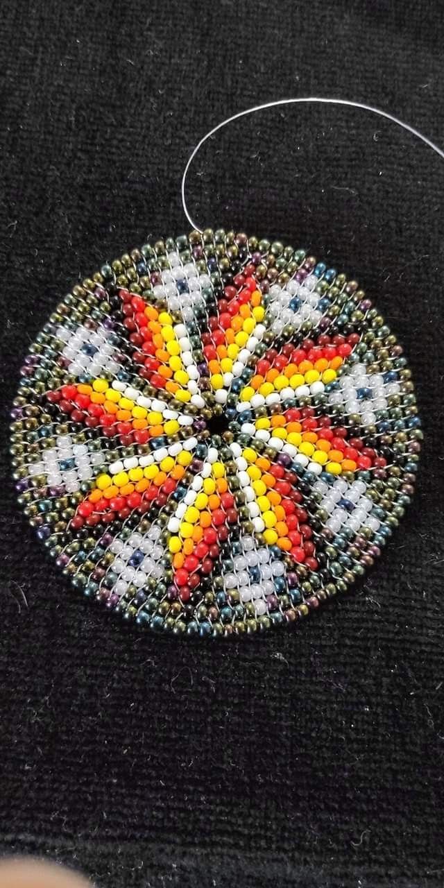 a colorful beaded ornament hanging on a black piece of cloth with thread