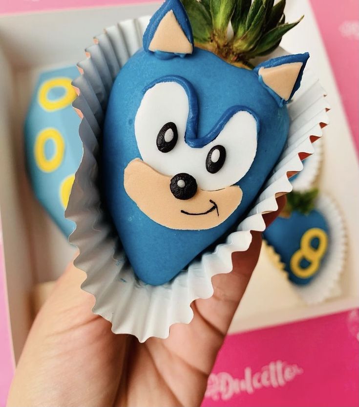 a hand holding a blue and white cupcake shaped like a hedgehog