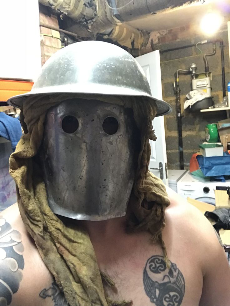 a man wearing a metal helmet with tattoos on his arm and chest is standing in a workshop