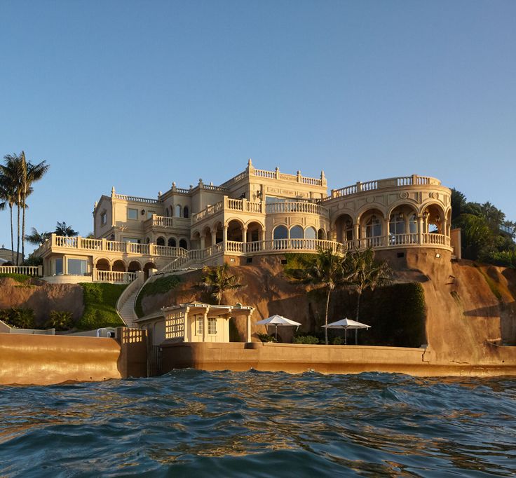 a large house sitting on top of a cliff next to the ocean with palm trees