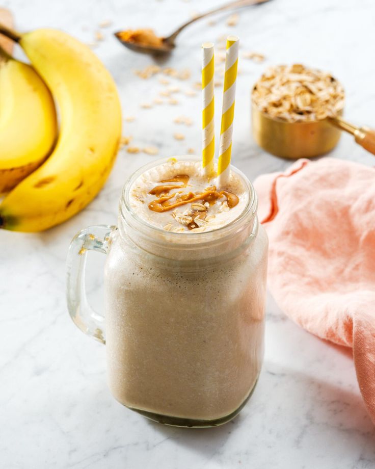 a smoothie in a mason jar with two straws next to it and bananas