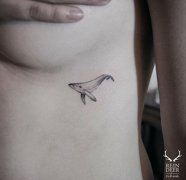 a woman's stomach with a small whale tattoo on her left side ribcage