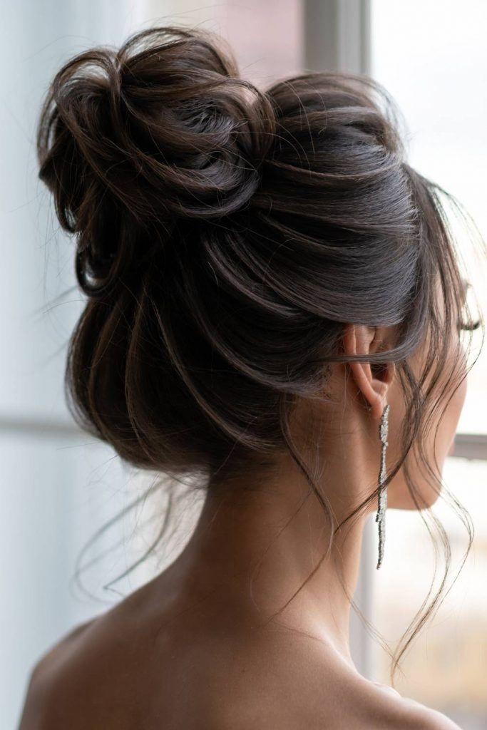 a woman with her hair in a low bun, wearing earrings and looking out the window