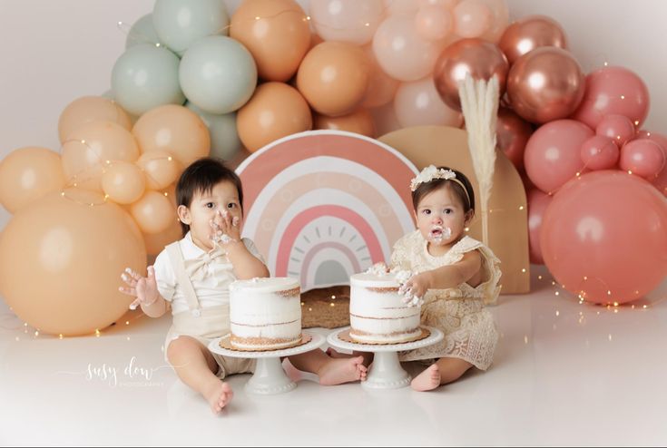 two babies are sitting in front of some balloons