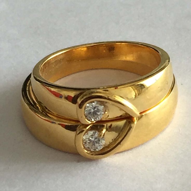 three gold rings with diamonds on them sitting on a white surface, the middle one has two smaller round stones in it