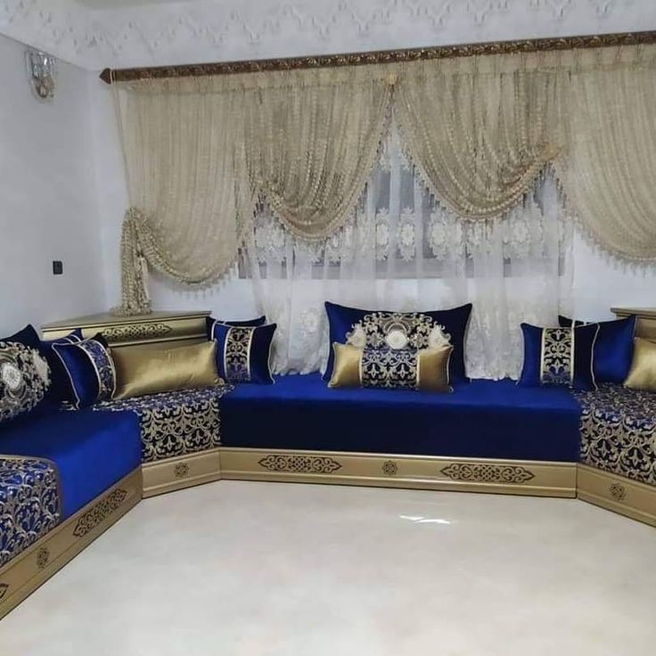 a living room with blue couches and gold pillows on the floor next to a window