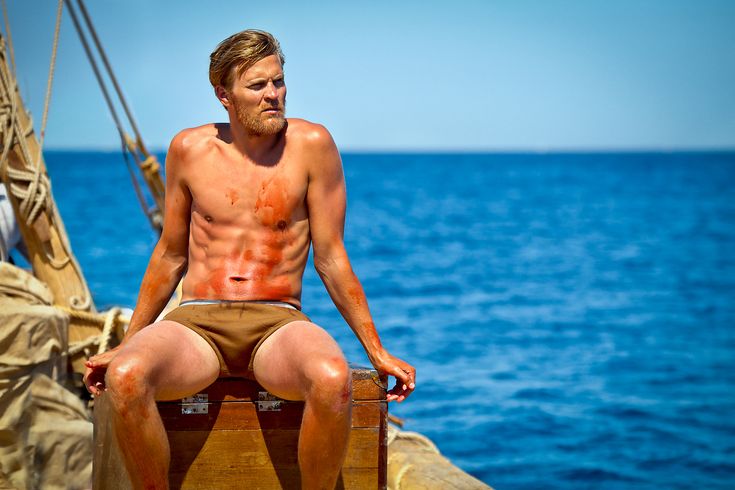 a shirtless man sitting on top of a wooden boat