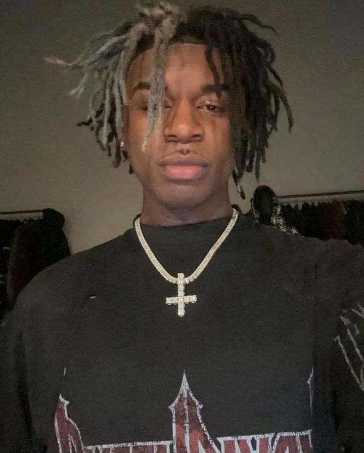 a young man with dreadlocks and a black t - shirt has a cross on his chest