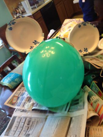 a green ball sitting on top of a table next to plates and newspapers with people in the background