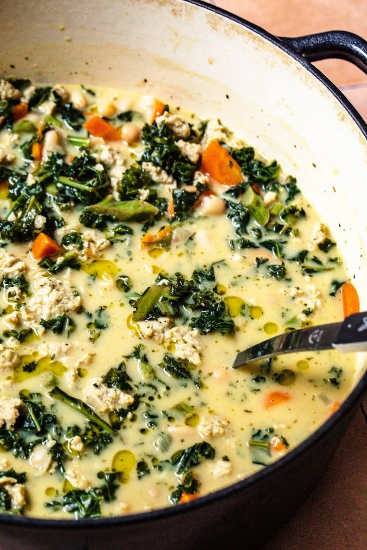 a pot filled with soup and vegetables on top of a wooden table next to a spoon