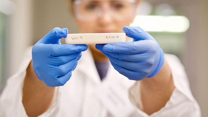 a woman in blue gloves holding up a small piece of white paper with writing on it