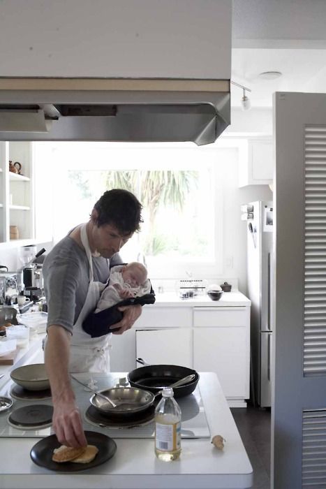 a man holding a baby while cooking in a kitchen