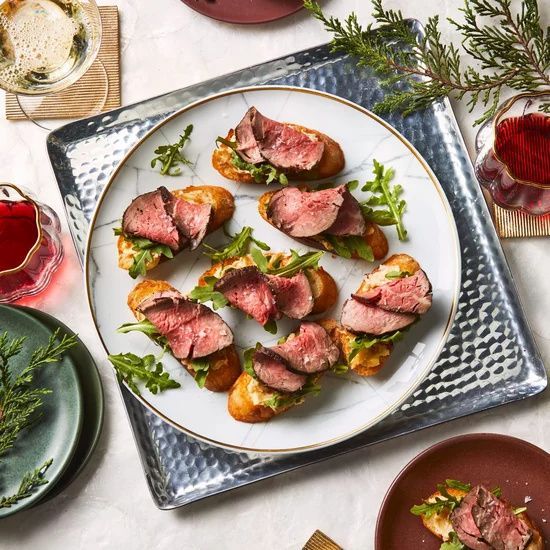 a plate filled with meat and vegetables on top of a white tablecloth next to silverware