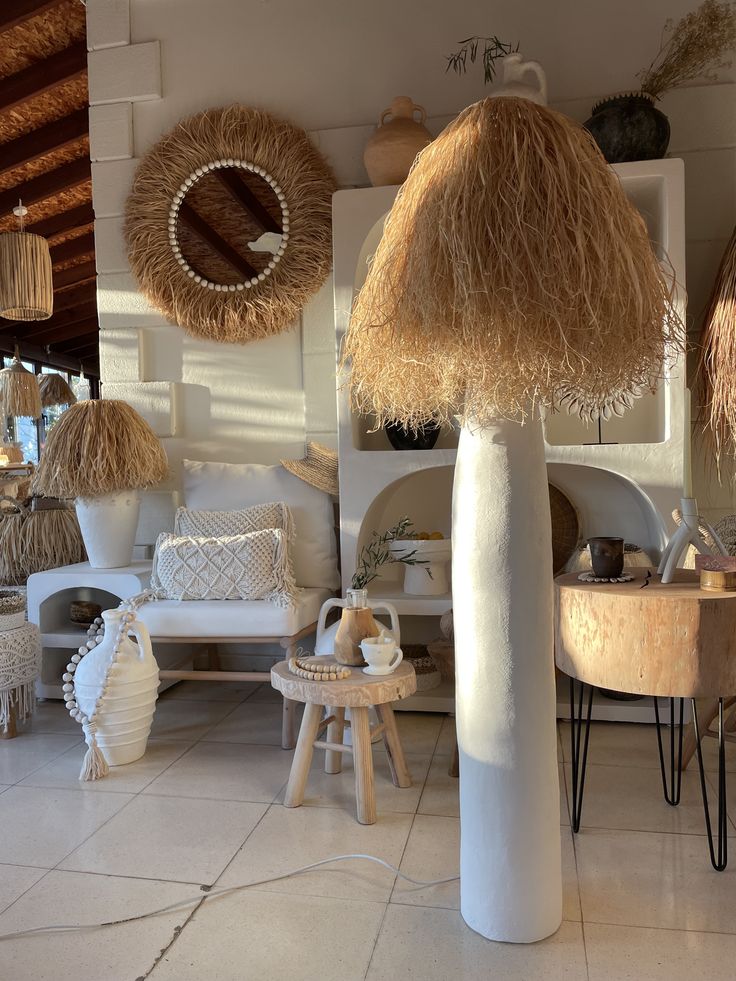 a living room filled with lots of white furniture and straw hats hanging from the ceiling