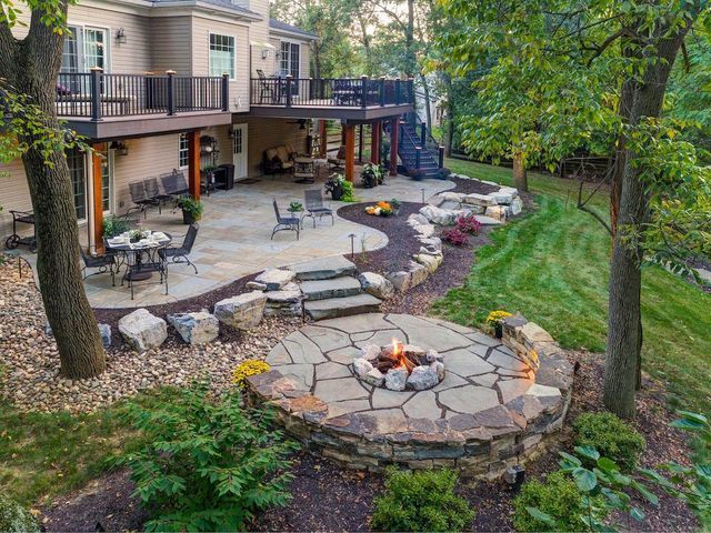 an outdoor patio and fire pit in the middle of a yard with landscaping around it