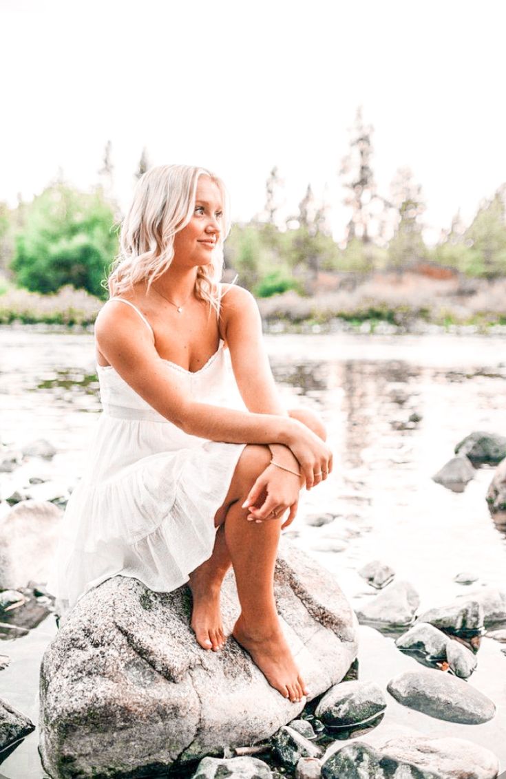 a woman sitting on top of a rock next to water