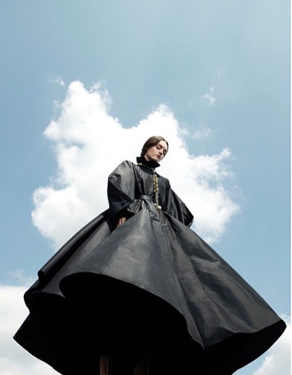 a woman in a black dress standing on top of a wooden pole under a cloudy blue sky