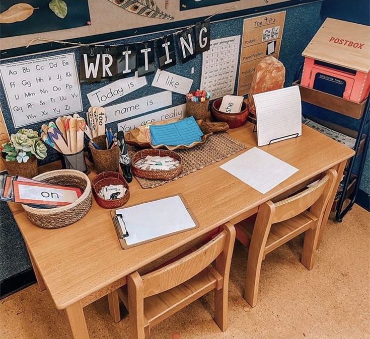 a wooden table topped with lots of books and writing materials next to a wall mounted bulletin board