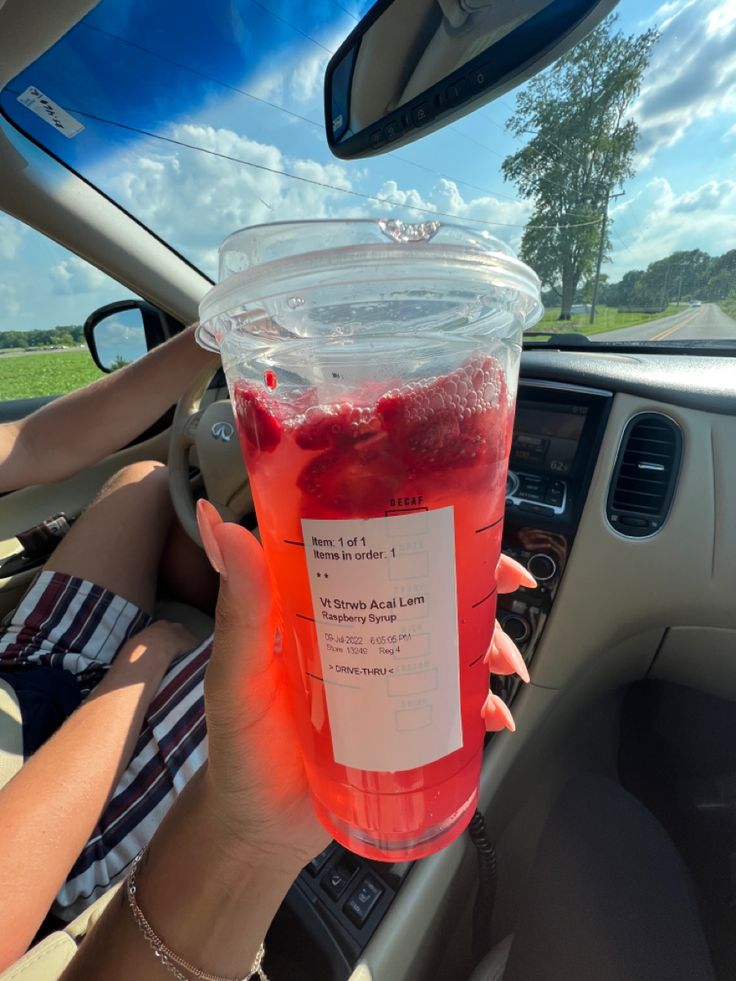 a person holding up a plastic cup filled with liquid in the back seat of a car