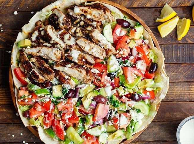 an overhead view of a salad with chicken, tomatoes, cucumber and olives