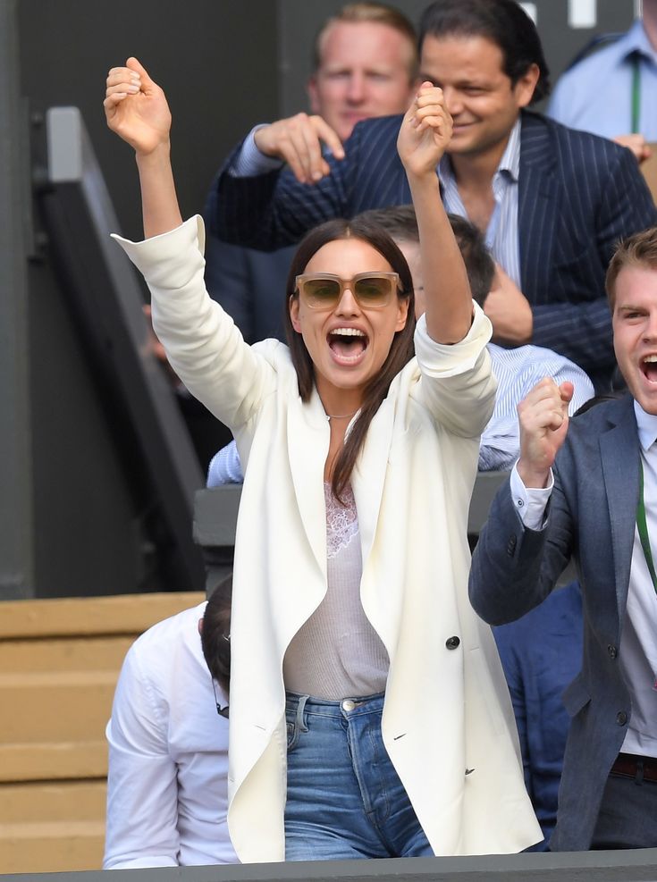 a woman holding her arms up in the air while standing next to other people at a tennis match