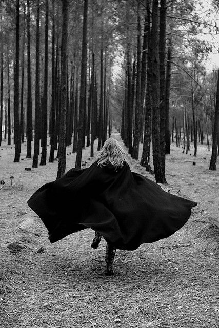 a woman in a black cloak is walking through the woods