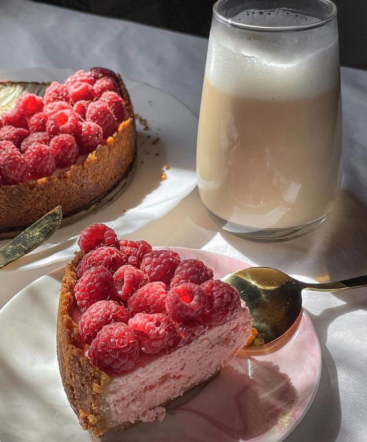 there is a piece of cake with raspberries on it next to a glass of milk