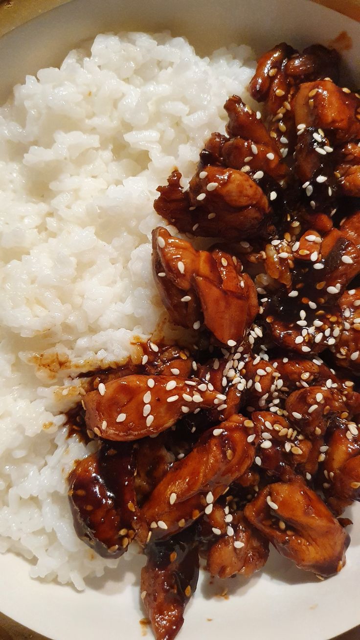 a white plate topped with rice covered in sesame seeds and chicken wings on top of it