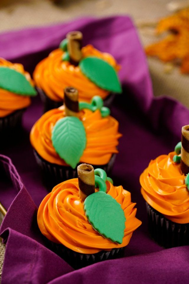 cupcakes with orange frosting and green leaves on them sitting on a purple cloth