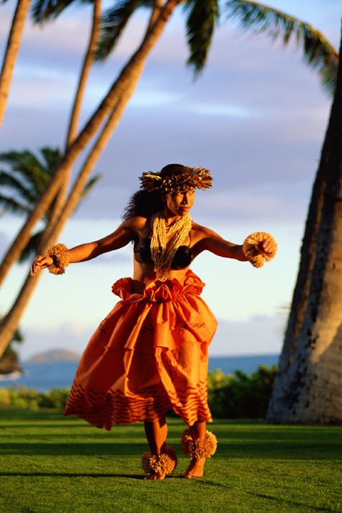 a woman in an orange dress is running through the grass with palm trees behind her