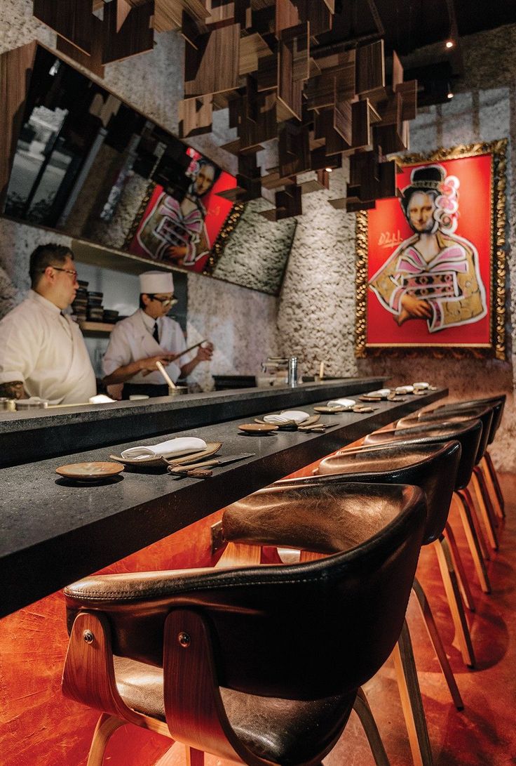 two men sitting at a bar with plates on the counter and chairs in front of them