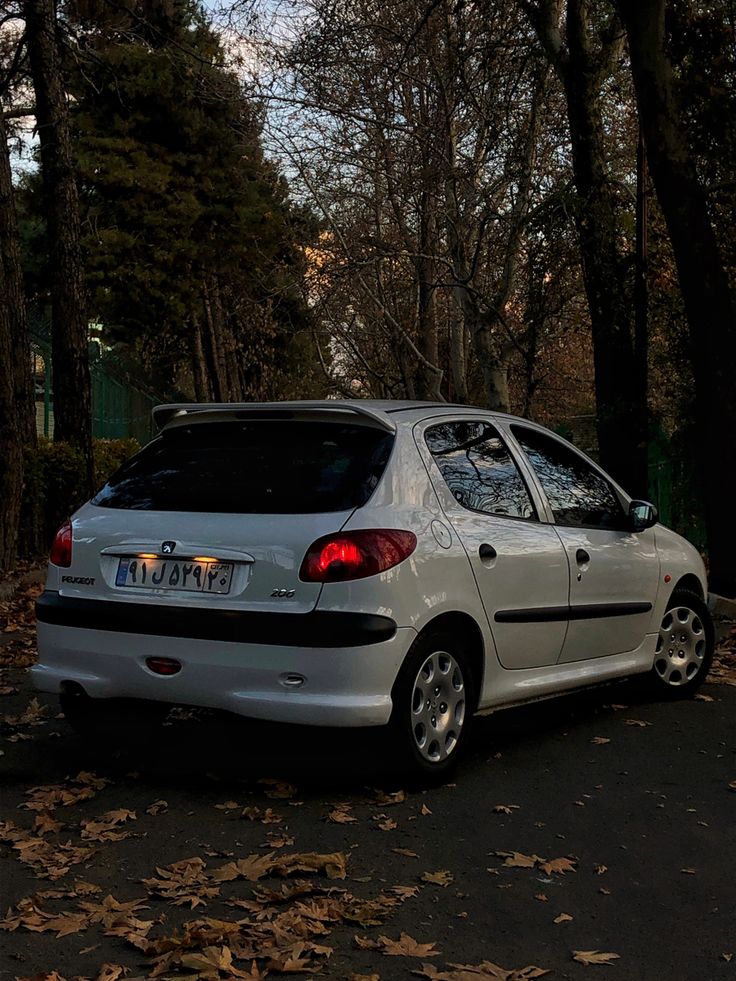 a small white car parked on the side of the road in front of some trees