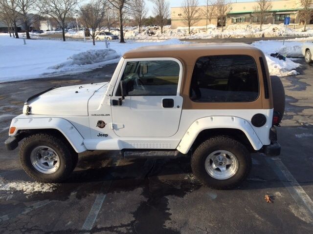 a white and brown jeep is parked in a parking lot with snow on the ground