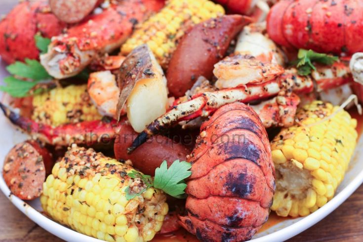 lobster, corn on the cob and potatoes are served in a white bowl with garnish