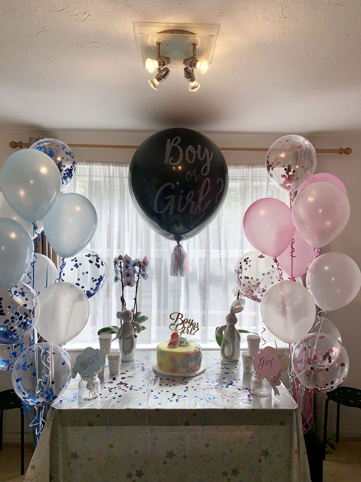 a table topped with balloons and cake next to a window