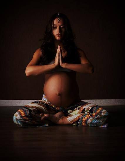 a pregnant woman sitting in the middle of a yoga pose with her hands clasped up