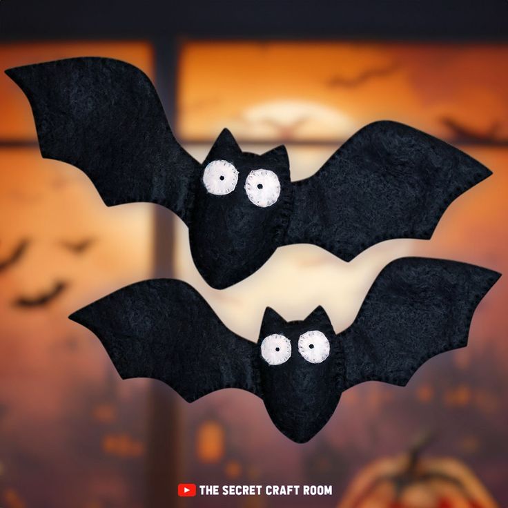 two black bats hanging from the ceiling in front of a window with pumpkins behind them