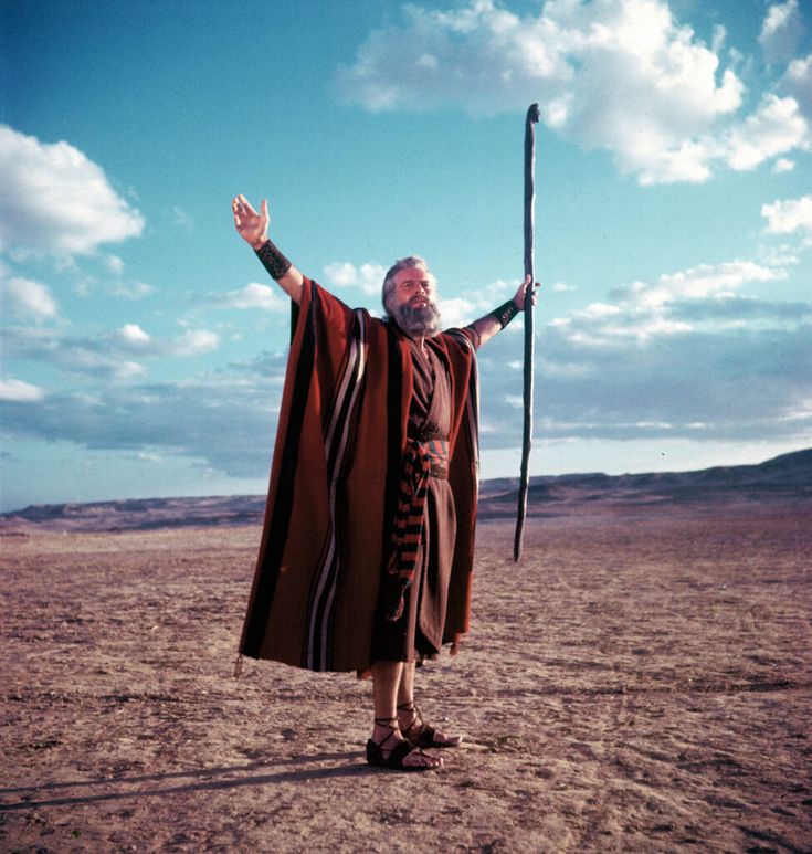 a man in a brown robe holding a stick and wearing a long red cape on top of his head