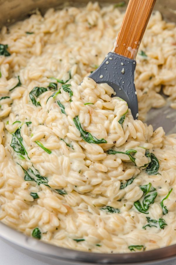 a ladle full of pasta and spinach being stirred with a wooden spatula