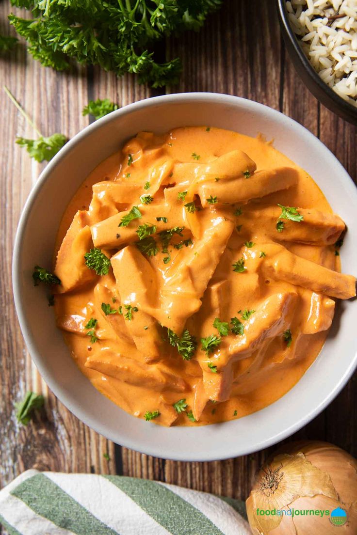 a white bowl filled with pasta and sauce on top of a wooden table next to some parsley