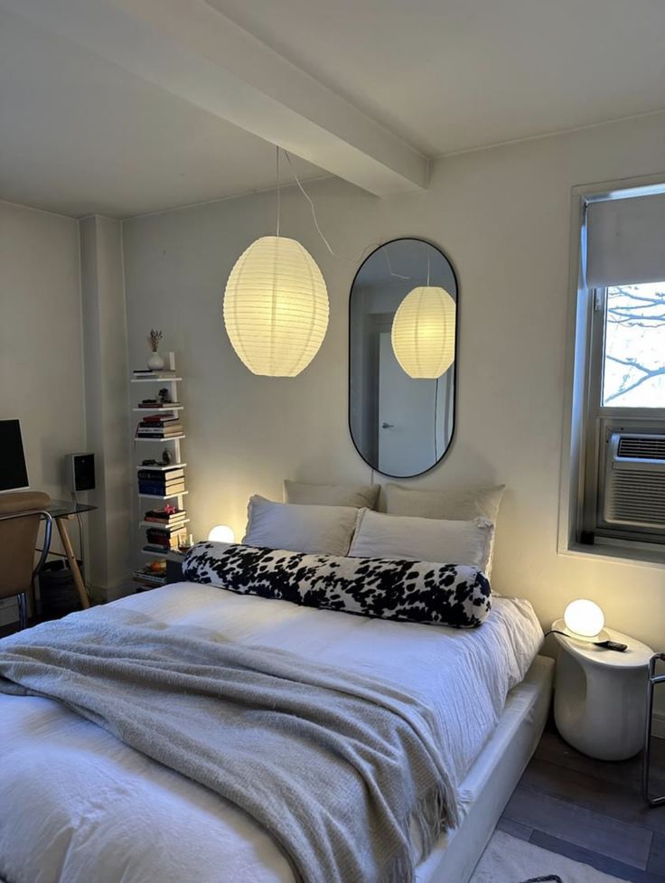 a bedroom with white bedding and two round lights hanging above the bed, along with a large mirror on the wall