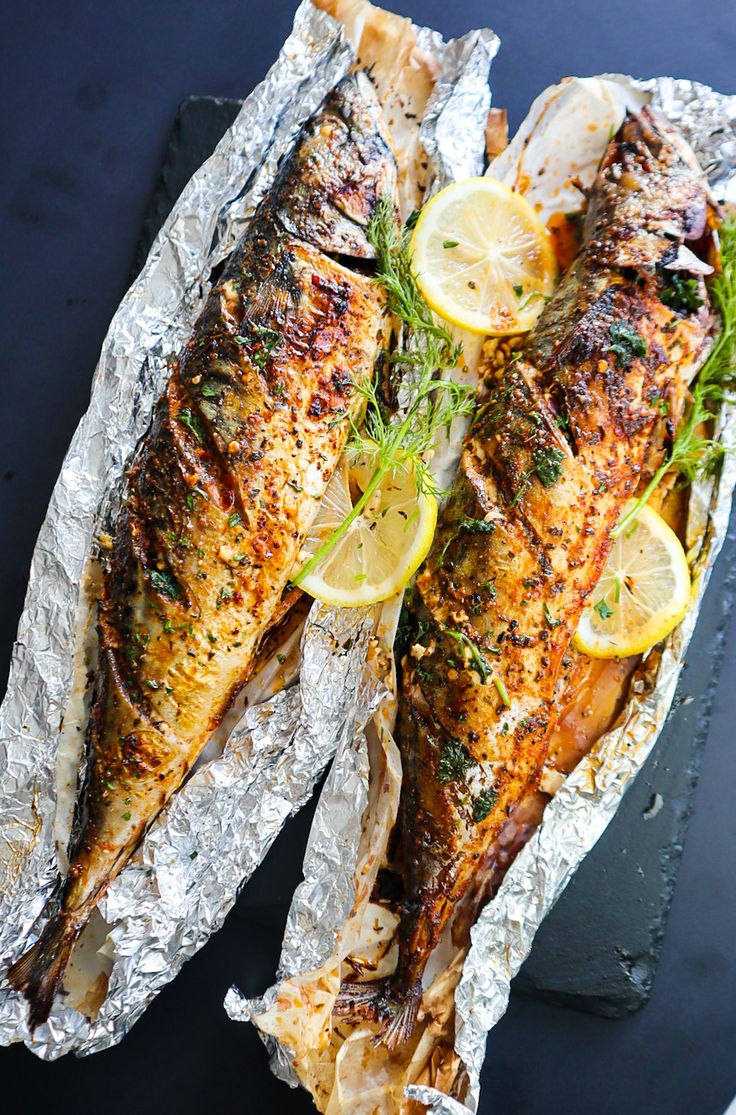 two fish on foil with lemon slices and herbs