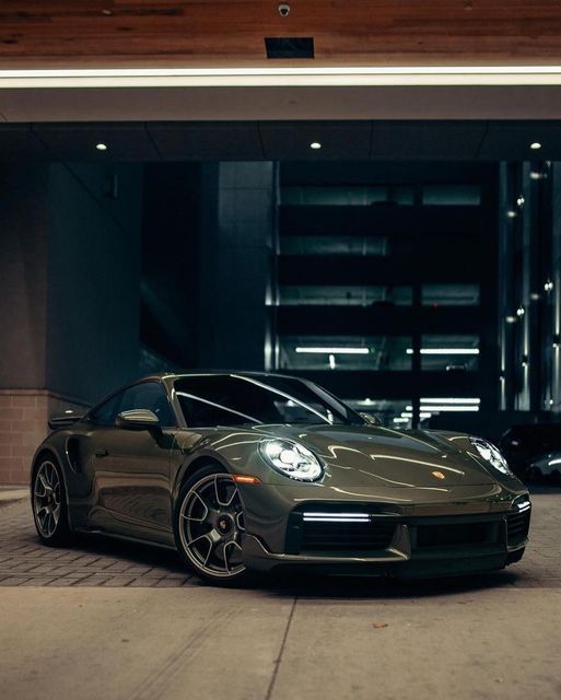 a green porsche parked in front of a garage with its lights on and the door open