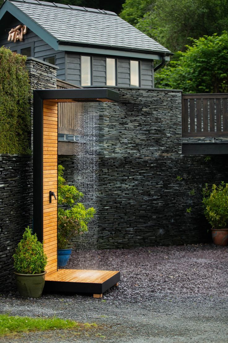 an outdoor shower in the middle of a gravel area next to a stone building and trees